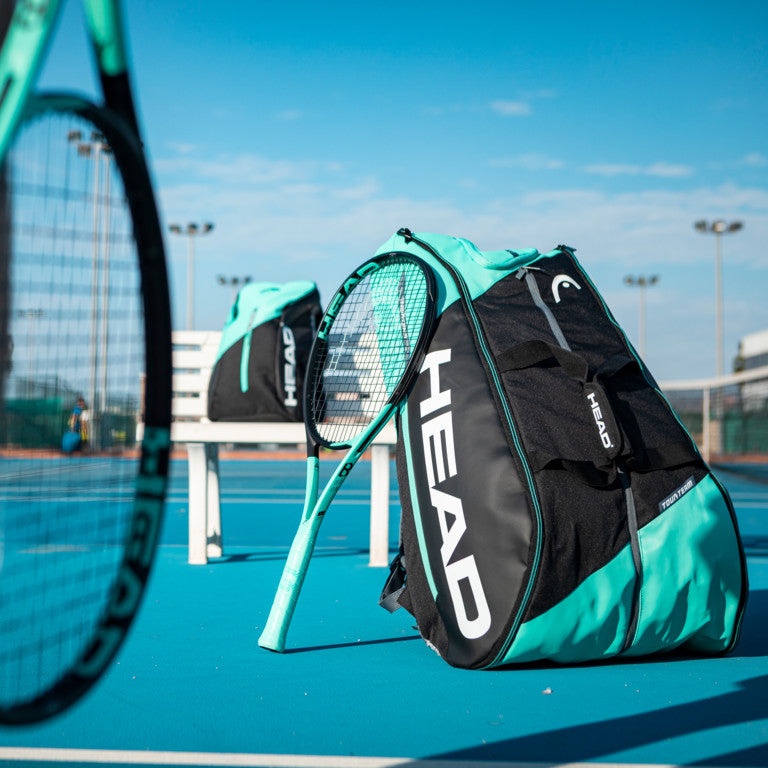 The Head Tour Team 12 Racket Monstercombi Tennis Bag in mint and black colour on a tennis court which is available for sale at GSM Sports.