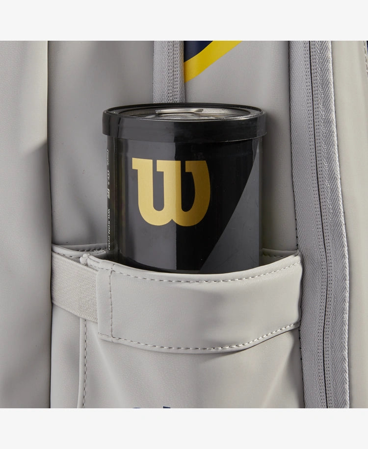 The Wilson US Open Tour Backpack in grey, blue and yellow with a tube of tennis ball inside for display purposes which is available for sale at GSM Sports.